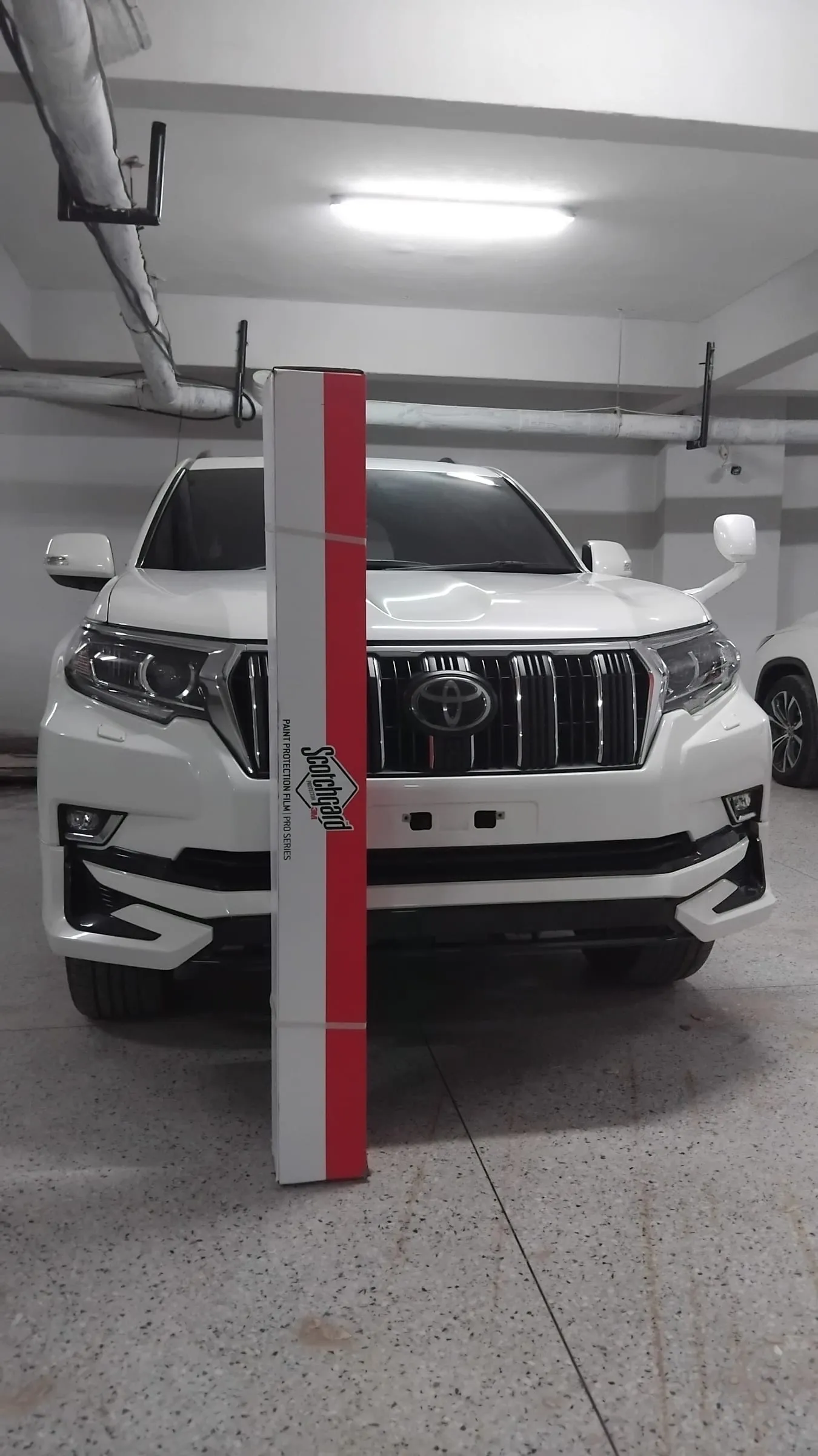 A roll of genuine 3M Scotchgard Paint Protection Film Pro Series in front of a white Toyota Land Cruiser Prado